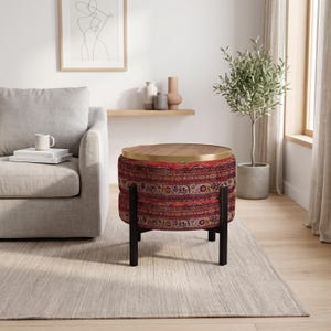 May include: A round ottoman featuring a vibrant red and multi-colored patterned fabric upholstery with a circular wooden top and a thin gold-toned metal rim. The piece is supported by four straight black legs, creating a stable base for this furniture.