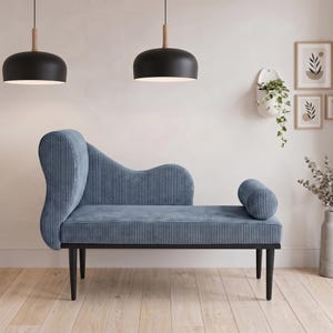 May include: A blue chaise lounge with a curved back and a cylindrical bolster. The lounge has a ribbed texture and sits on black legs. Two black pendant lights hang above the lounge.