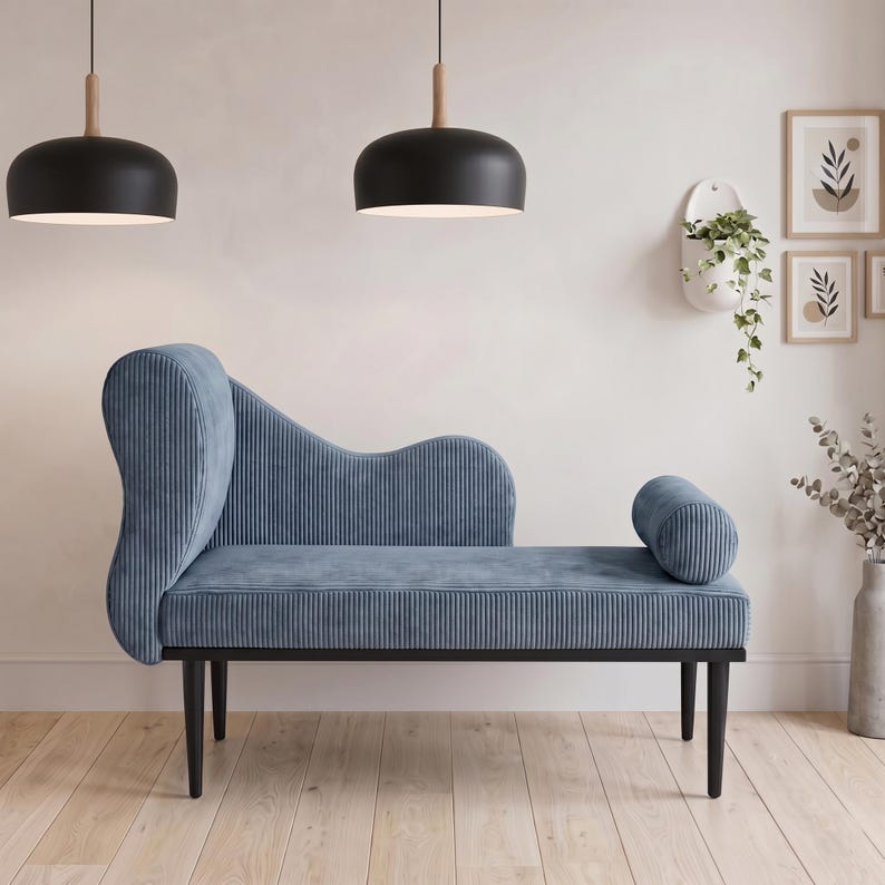 May include: A blue chaise lounge with a curved back and a cylindrical bolster. The lounge has a ribbed texture and sits on black legs. Two black pendant lights hang above the lounge.