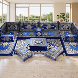 Può includere: Un set di sedute modulari con un motivo geometrico blu e bianco. Il set include diversi cuscini e un pouf centrale, disposti su un tappeto a fantasia. Il design presenta una combinazione di blu, bianco e nero.