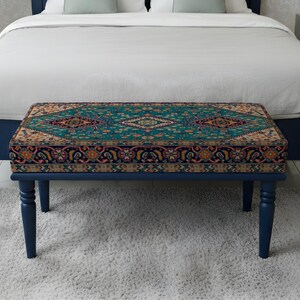 May include: A rectangular bench with a patterned top and dark blue legs. The bench is positioned in front of a bed with a white duvet. The bench's top features a teal, orange, and beige geometric design.