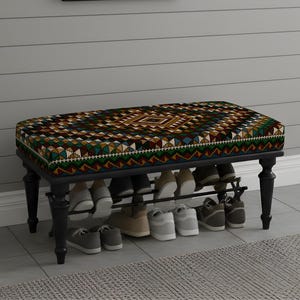 May include: A black shoe bench with a patterned cushion in shades of brown, green, and blue. The bench has a shoe rack underneath, holding several pairs of shoes. The legs are black and turned.