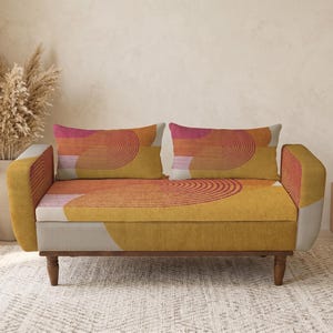 Pode incluir: Um sofá de dois lugares com um padrão geométrico em tons de amarelo, laranja e rosa. O sofá tem pernas de madeira e duas almofadas retangulares a condizer. O design é moderno e elegante, adequado para decoração de casa.