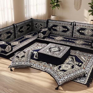 May include: A modular, low-profile seating set with a dark blue and cream geometric pattern. The set includes a corner sofa, cushions, a square ottoman, and a rug, all with matching designs. The pieces are arranged on a light wood floor.