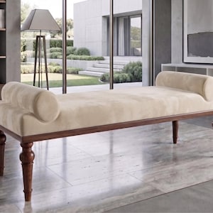 May include: A rectangular bench featuring a cream-coloured upholstered seat with two matching cylindrical bolster pillows at each end. The base is constructed from dark brown wood with four turned legs that provide structural support.