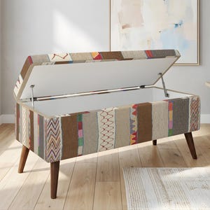 Könnte beinhalten: Eine rechteckige Aufbewahrungsbank mit Klappdeckel, die ein Patchwork-Design in verschiedenen Farben wie Beige, Braun, Rot und Blau aufweist. Die Bank hat dunkle Holzbeine und ist offen, wodurch ein weißer Innenraum sichtbar wird.