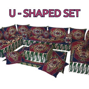 Op de afbeelding: Een U-SHAPED SET van vloerkussens met een donkerblauwe, rode en groene patroonstof met complexe geometrische ontwerpen. De set bevat rugleuningen, vloerkussens en vierkante kussens, die allemaal qua kleur en patroon op elkaar zijn afgestemd.
