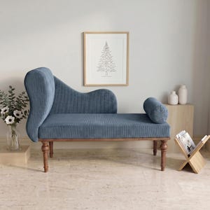May include: A blue corduroy chaise lounge with a curved back and a cylindrical bolster pillow. The wooden frame has turned legs. A framed line drawing of a tree hangs on the wall behind the chaise lounge.