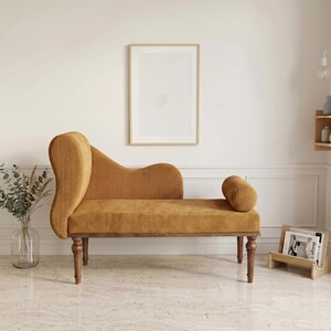 K&ouml;nnte beinhalten: Eine senfgelbe Cord-Chaiselongue mit geschwungener R&uuml;ckenlehne und einem zylindrischen Kissen. Die Holzbeine und der Rahmen tragen die Sitzfl&auml;che. Ein gerahmter geometrischer Druck h&auml;ngt an der Wand hinter der Chaiselongue.