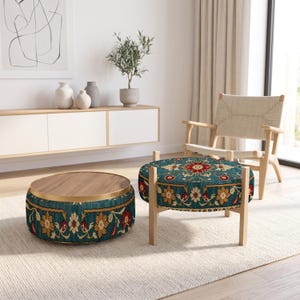 May include: A round coffee table with a wooden top and a teal fabric base featuring a floral pattern, paired with a matching round ottoman on light wooden legs. The teal fabric displays a repeating design of red and beige flowers with green leaves.