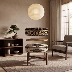 May include: A round ottoman featuring a dark, intricate floral pattern on its top and a cream-colored base with a geometric medallion design. The piece is supported by a dark wood cross-leg frame and includes a circular wooden tray insert.