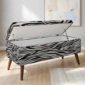 May include: A zebra-print storage bench with a hinged lid, showcasing a black and white striped pattern. The bench has four dark wooden legs and a white interior. The lid is open, revealing the storage space.