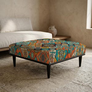 Peut inclure: Un pouf carré avec un cadre noir et quatre pieds noirs. Le dessus est recouvert d'un motif patchwork coloré avec des motifs géométriques orange, turquoise et jaunes. Le pouf est placé dans un salon.