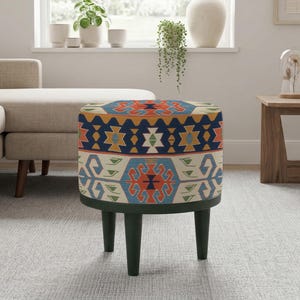 Peut inclure: Un pouf rond rembourré avec un motif géométrique coloré dans les tons de bleu, orange et vert. Le pouf a des pieds vert foncé et est placé dans un salon.