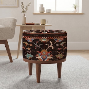 Könnte beinhalten: Ein runder Hocker mit einem dunkelbraunen, gemusterten Oberteil mit floralen Designs in Rot-, Blau- und Grüntönen. Der Hocker hat eine Holzbasis und Beine und verleiht dem Raum einen Hauch von Eleganz.