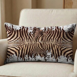 May include: Rectangular decorative pillow with a zebra print design. The pillow features a pattern of brown and tan zebra stripes against a white background with a distressed, textured effect. The pillow is placed on a beige sofa.