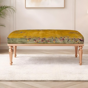 May include: A decorative bench with a mustard yellow cushion featuring a floral design in shades of red, green, and purple. The bench has four wooden legs with a light brown finish. The bench is approximately 48 inches long.