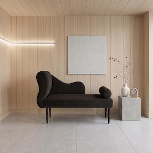 May include: A modern interior scene featuring a dark brown chaise lounge with a curved back and cylindrical bolster. The room has light wood paneling, a white square artwork, and a small side table with a vase and clock.