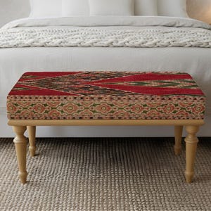 May include: A decorative bench with a rectangular seat featuring a red, black, and green patterned design. The bench has four turned wooden legs and is placed in front of a bed with white bedding. The bench is approximately 122 cm long.