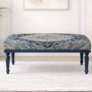 Puede incluir: Un banco azul marino con una parte superior estampada en tonos de azul, beige y crema. El banco tiene cuatro patas torneadas y está colocado sobre una alfombra blanca. El banco es un mueble decorativo.