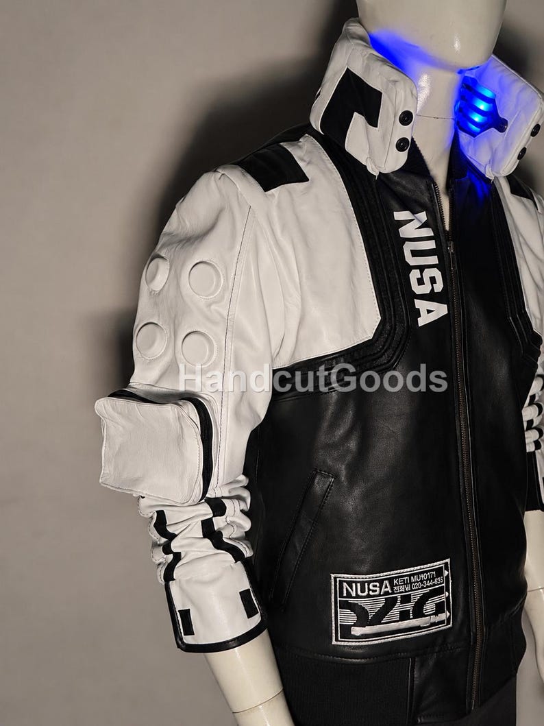 May include: A black and white jacket featuring a high collar with blue LED lighting, the text NUSA printed on the chest, a white sleeve with circular embossed details, a small attached pouch, and a rectangular patch with NUSA text at the hem.