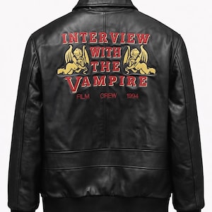 Puede incluir: Chaqueta bomber de cuero negro con el texto "INTERVIEW WITH THE VAMPIRE" en letras rojas y doradas en la espalda. La chaqueta tiene cuello, puños y dobladillo de canalé. El texto incluye las palabras "FILM", "CREW" y el año "1994".