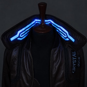 Puede incluir: Una chaqueta de color marr&oacute;n oscuro con un cuello alto que presenta tiras de luz azul brillante integradas. La chaqueta incluye un parche rectangular en el pecho con el texto CRYSTAL JOCK impreso en letras blancas y una cremallera frontal.