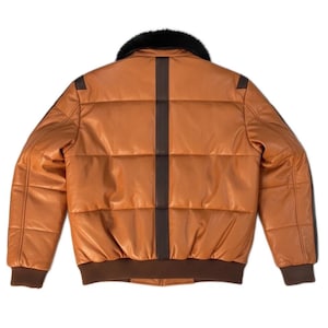 May include: A tan leather bomber jacket with a black fur collar. The jacket has a brown vertical stripe down the back and brown trim on the cuffs and waist. The jacket is quilted and has a classic bomber style.