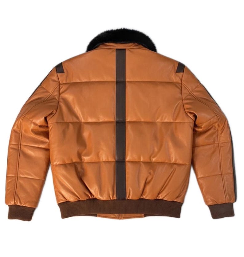 May include: A tan leather bomber jacket with a black fur collar. The jacket has a brown vertical stripe down the back and brown trim on the cuffs and waist. The jacket is quilted and has a classic bomber style.