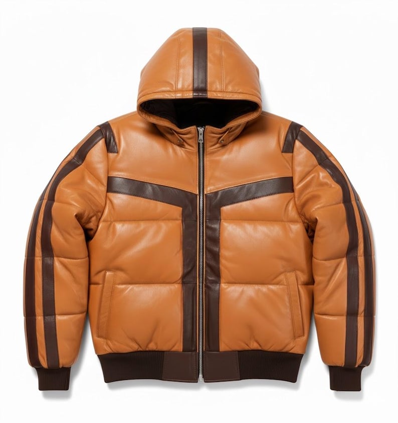 May include: A tan leather puffer jacket with a hood and dark brown accents. The jacket features a zip-up front, two front pockets, and dark brown stripes on the sleeves and hood. The jacket has a ribbed hem and cuffs.