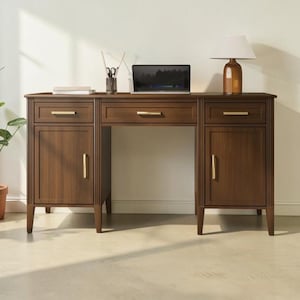 Può includere: Una scrivania in legno scuro con un cassetto centrale, due armadietti laterali e due cassetti più piccoli sopra gli armadietti. La scrivania presenta dettagli scanalati verticali sui pannelli laterali e maniglie dorate. Un portatile, una lampada e un portapenne sono appoggiati sopra.