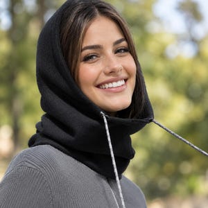 May include: A black fleece hood with a high neck covering, featuring a drawstring closure with thin, light-colored cords. The hood is designed to fit snugly around the head and neck, providing warmth and coverage for the upper body area.