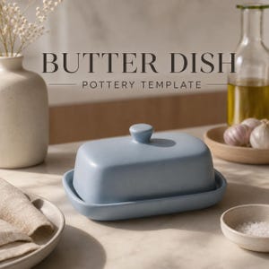 Peut inclure: Un beurrier en céramique bleu clair avec un couvercle et un petit bouton. Le plat repose sur une base assortie. Les mots "BUTTER DISH POTTERY TEMPLATE" sont imprimés au-dessus du plat. L'arrière-plan comprend un vase, une bouteille et un petit bol.