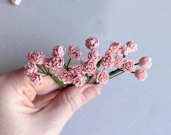 May include: A bunch of small, pink paper flowers with green stems. The flowers are clustered together and have a delicate, ruffled appearance.