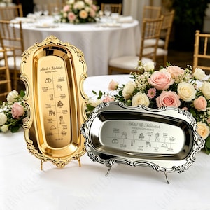 Peut inclure: Deux plateaux décoratifs pour le déroulement d'un mariage. L'un est doré, l'autre argenté. Les deux ont des bords ornés et sont soutenus par de petits supports. Les plateaux affichent un calendrier de mariage avec des icônes et du texte.