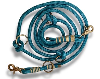 May include: A teal blue double dog leash with gold hardware and a cream colored accent. The leash is made of rope and has two clips.