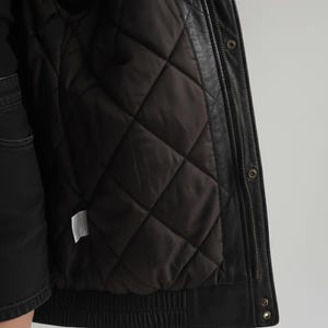 Close-up of quilted lining and stitching details on a women’s oversized sheepskin leather jacket. The leather texture, inner padding, and bomber coat structure highlight warmth, durability, and high-quality craftsmanship. Perfect winter outerwear choice with both fashion and comfort appeal for cold weather styling.
