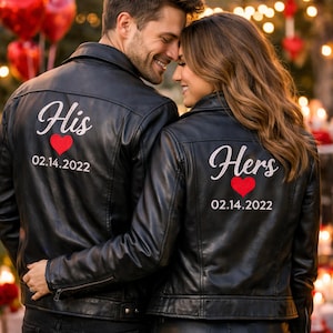 以下が含まれることがあります： 「His」と「Hers」の白い筆記体、赤いハート、日付02.14.2022がそれぞれプリントされた、お揃いの黒い革のジャケット。 ジャケットはカップルが着用しており、背景にはぼやけた光とハート型の風船が写っています。