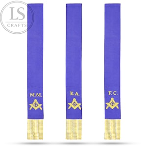 May include: Three royal blue Masonic sashes with gold fringe. Each sash features gold embroidered symbols and initials: M.M., E.A., and F.C. The sashes are vertically oriented against a white background.