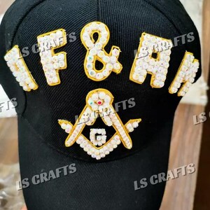 Könnte beinhalten: Schwarze Baseballkappe mit den Buchstaben "F & A" und einem Freimaurersymbol, alle mit weißen und goldenen Strasssteinen verziert. Auf der Kappe steht auch der Text "LS CRAFTS".
