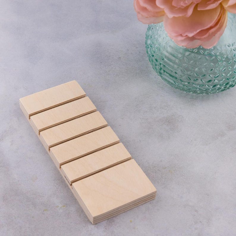 Op de afbeelding: Een houten displaystandaard met vijf sleuven om kleine items te presenteren, zoals sieraden of andere accessoires. De standaard is gemaakt van licht hout en heeft een gladde, gepolijste afwerking.