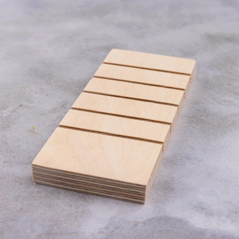 Op de afbeelding: Een houten displaystandaard met zes sleuven om kleine items te organiseren. De standaard is gemaakt van licht hout en heeft een natuurlijke afwerking.