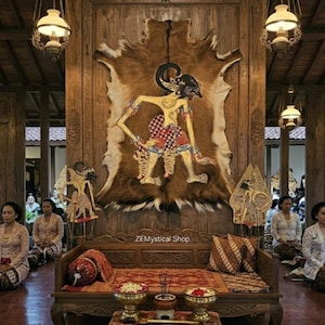 Puede incluir: Un banco de madera con un tapiz de piel animal en la pared que muestra una figura de marioneta de sombra Wayang Kulit, flanqueada por dos más pequeñas. El banco tiene cojines rojos estampados y dos cuencos de latón con flores, con el texto ZEMystical Shop.