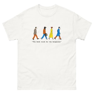 Puede incluir: Camiseta blanca con una ilustración humorística de cuatro figuras con abrigos y sombreros, caminando en fila. Las figuras son de varios colores, con el texto "The birds work for the bougeoisie" debajo.