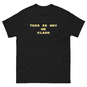 May include: Black t-shirt with the text "THIS IS WHY WE CLASH" in a yellow, blocky font. The shirt is a classic crew neck style, likely made of cotton or a similar fabric. The text is centered on the chest.