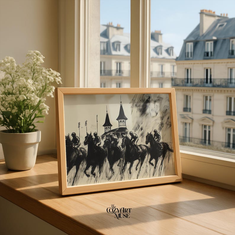 May include: A framed black and white print of a horse race, featuring jockeys on horseback. The artwork is set in a light wooden frame and rests on a wooden surface. The Cozy Art Muse logo is visible in the bottom right corner. A potted plant and a window with a city view are in the background.