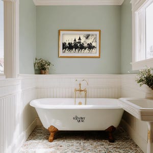 May include: A bathroom with a white clawfoot bathtub, gold fixtures, and a framed black and white equestrian print. The walls are painted a soft green, and the floor is tiled with small, multicolored stones.