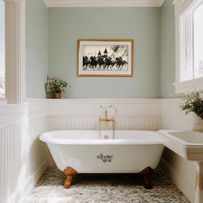 May include: A bathroom with a white clawfoot bathtub, gold fixtures, and a framed black and white equestrian print. The walls are painted a soft green, and the floor is tiled with small, multicolored stones.