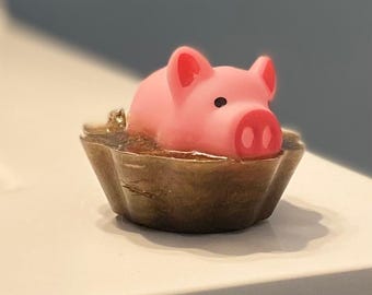 May include: A pink pig figurine is sitting in a brown, textured, ceramic dish. The pig has a black eye and a pink snout.