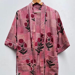 May include: A pink and white floral patterned robe with a white trim. The robe has a tie belt and short sleeves.